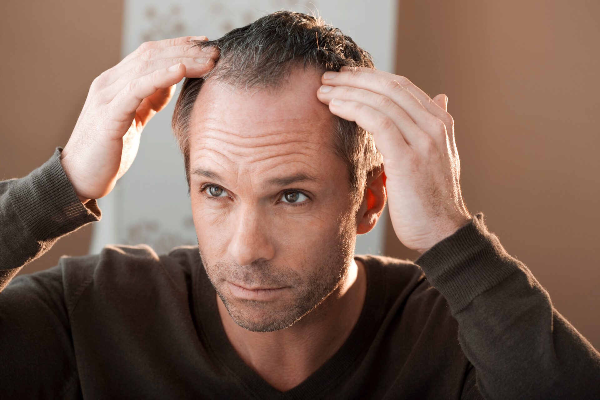 Man is looking at himself in the mirror and examining for hair loss and thinking about hair myths.